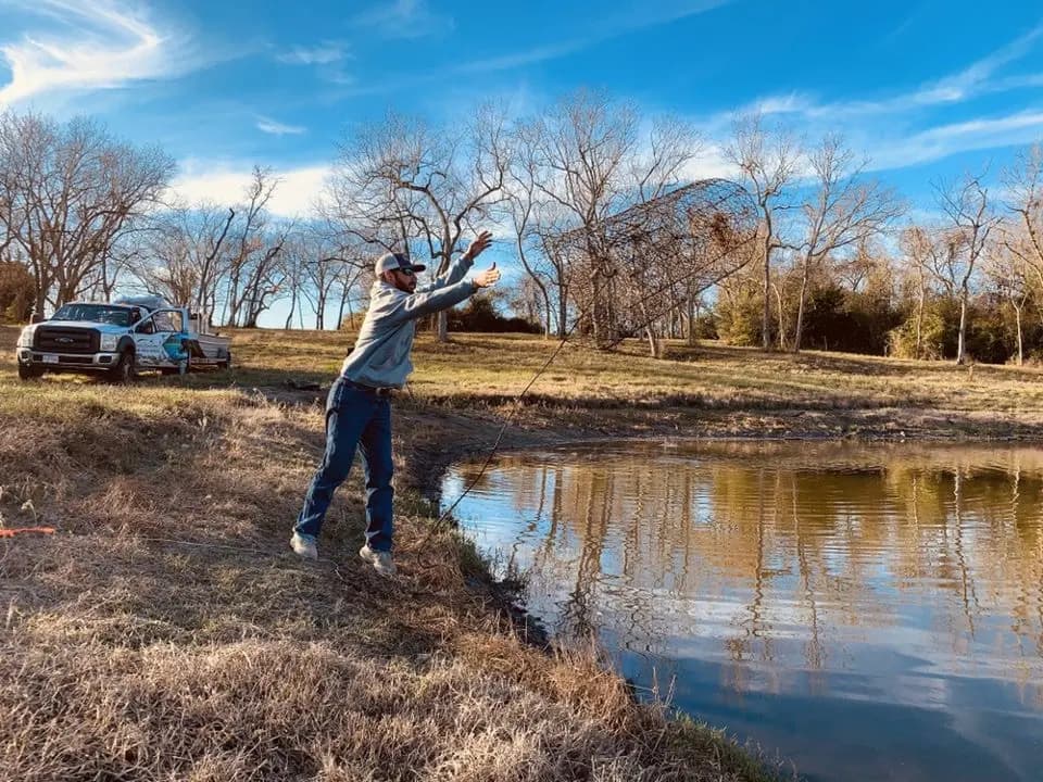 A Shoreline Trapping crew member setting a trap at a Texas pond at golden hour